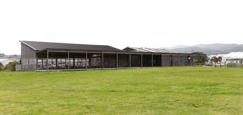 a empty field in front of two long low sheds with a verandah